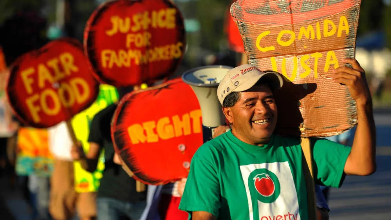 A line of protesting farm workers holding cardboard signs that say comida