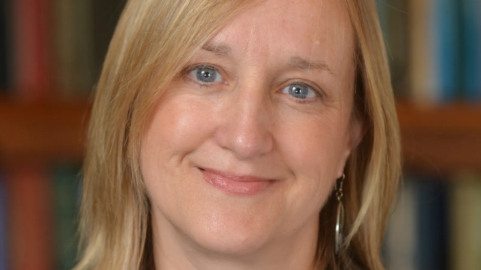 A light skinned woman with blonde hair and a blue shirt looks directly at the camera