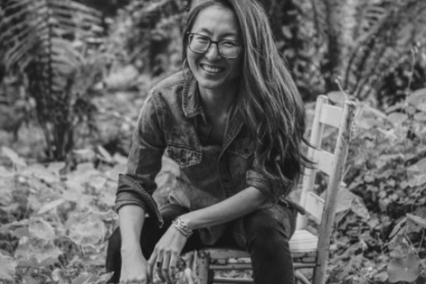 Black and white image of Mia Mingus sitting on a wooden chair in a jungle setting
